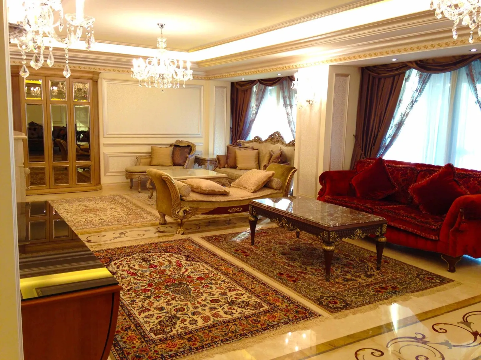 Formal living room with cream and gold upholstered seating, patterned marble floor and matching table lamps either side of a mirrored cabinet